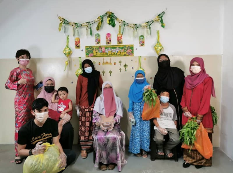 Tan (far left) and Norhayati (seated) with her eight children who were happy after selecting their favourite Hari Raya clothes. — Picture via Nicole Tan Lee Koon
