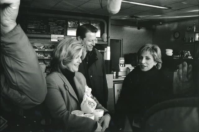 <p>NBC News</p> Andrea Mitchell stands in a Dunkin' Donuts with Al and Tipper Gore on the 1992 presidential campaign trail