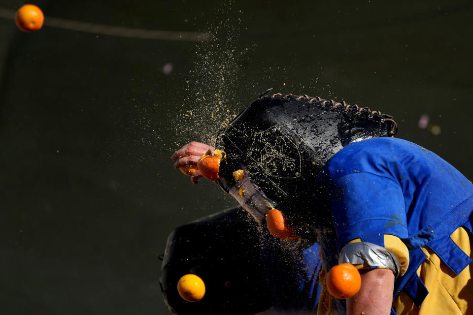 People wearing protection helmets and costumes pelt each other with oranges during the 'Battle of the Oranges" part of Carnival celebrations in the northern Italian Piedmont town of Ivrea, Italy, Tuesday, Feb. 13, 2024. (AP Photo/Antonio Calanni)