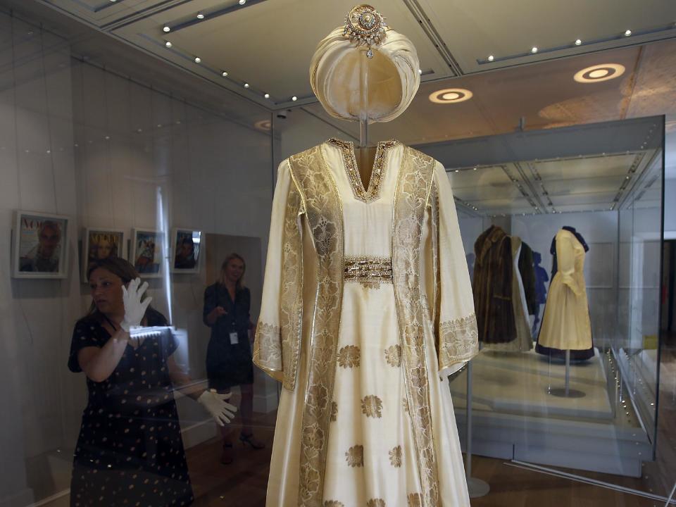 In this photo taken Monday, July 1, 2013, an employee cleans the glass cabinet showing a turban dress worn by Princess Margaret, at the Fashion Rules exhibition at Kensington Palace in London. Opening on 4 July, a new glamorous exhibit at Kensington Palace showcases how the styles of three royal ladies; Queen Elizabeth II, her sometimes risque sister Margaret, and the glamorous Princess Diana, each reflected and influenced the trends of their fashion heyday. (AP Photo/Frank Augstein)