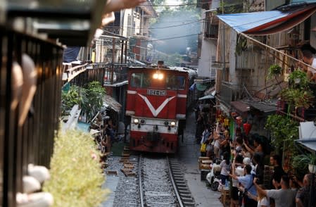 Tourists take photos as a train comes down the track along a street in the Old Quarter of Hanoi, Vietnam