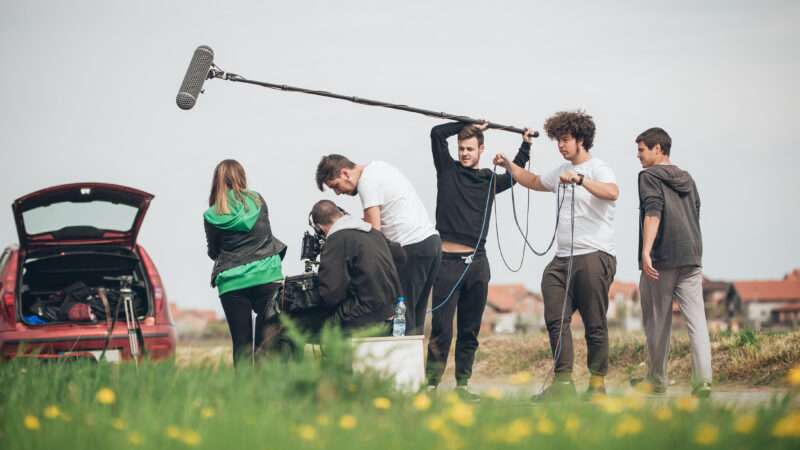 A group of young people shoot a film in an open field.
