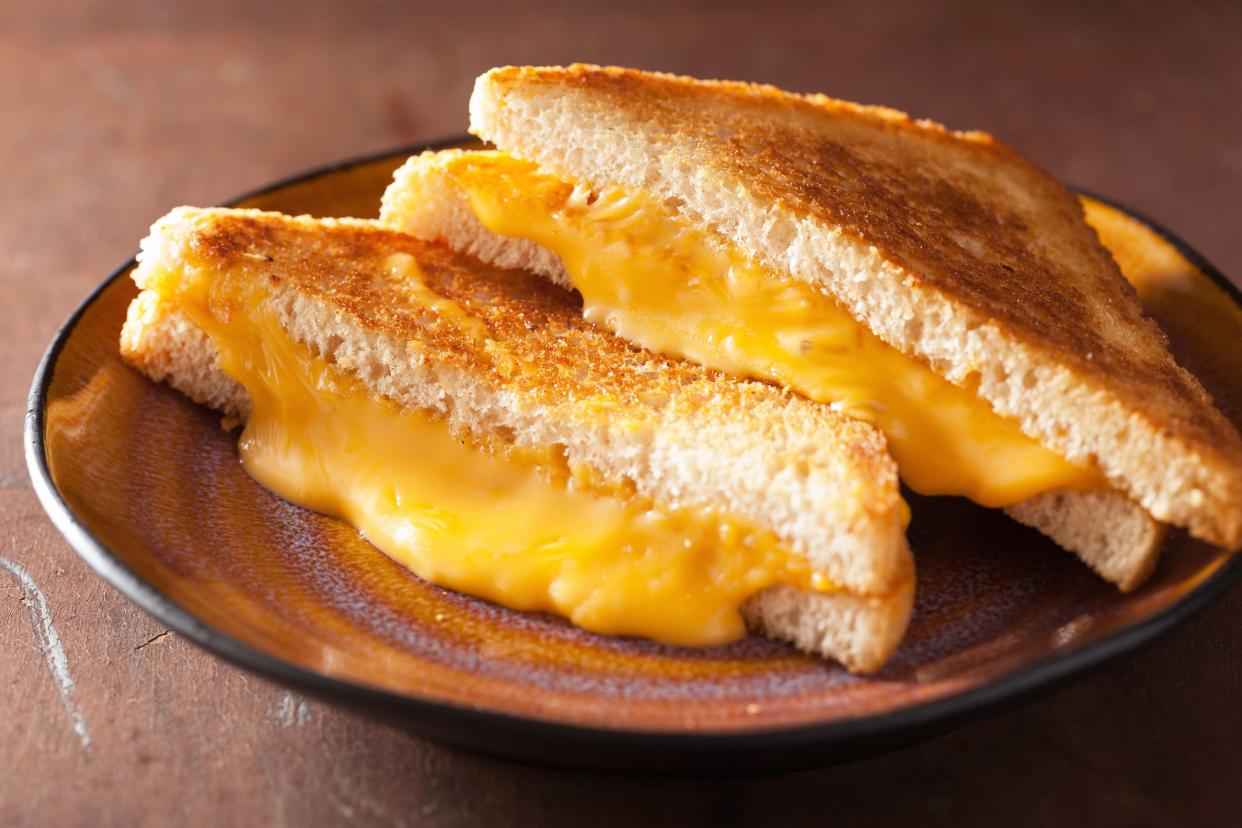 Two halves of grilled cheese sandwich on a purple and orange ceramic plate, selective focus, on a wooden table