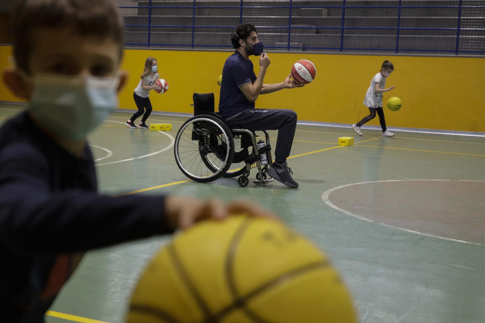 Adolfo Damian Berdun, of Argentina, a professional player and captain of the Argentine basketball Paralympic team, teaches children basketball at a primary school in Verano Brianza, outskirt of Milan, Italy, Tuesday, May 11, 2021. Four second-grade classes in the Milan suburb of Verano Brianza have been learning to play basketball this spring from a real pro. They also getting a lesson in diversity. Their basketball coach for the last month has been Adolfo Damian Berdun, an Argentinian-Italian wheelchair basketball champion. Berdun, 39, lost his left leg in a traffic accident at ag 13 in his native Buenos Aires, and he has visited many schools over the years to discuss how he has lived with his disability.(AP Photo/Luca Bruno)