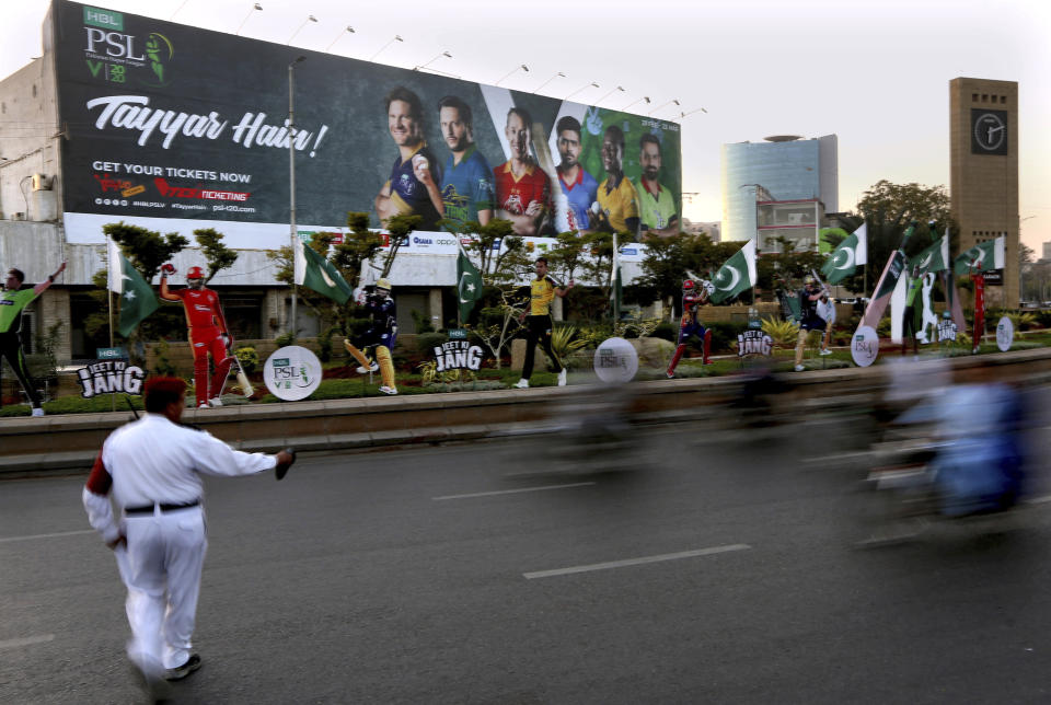 In this Saturday, Feb. 15, 2020, photo, a traffic police officer control traffic infant of huge billboard of cricketers displays along roadside in preparation of the upcoming Pakistan Super League, in Karachi, Pakistan. Security concerns stopped foreign cricketers from touring Pakistan four years ago when the country's premier domestic Twenty20 tournament was launched, forcing organizers to stage the event on neutral turf in the United Arab Emirates. When the 2020 edition of the PSL starts in Karachi on Thursday, Darren Sammy of the West Indies and Shane Watson of Australia will be among 36 foreign cricketers involved in the six franchises. (AP Photo/Fareed Khan)