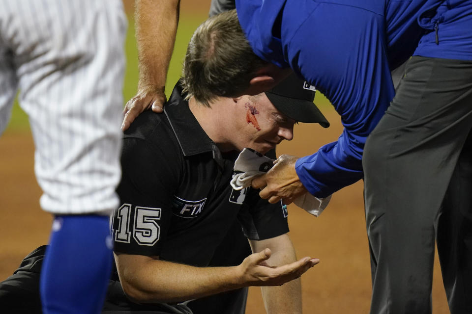 First base umpire Junior Valentine is checked by a trainer after he was hit by a thrown ball during the second inning of a baseball game between the New York Mets and the St. Louis Cardinals, Monday, Sept. 13, 2021, in New York. (AP Photo/Frank Franklin II)