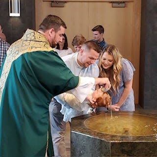 Colt Cramer gets baptized at St. Mary in Hales Corners by Father Aaron Laskiewicz while wearing the family's traditional baptismal dress. Colt's father, Alex Cramer, and mother, Kayla Cramer, happily look on.