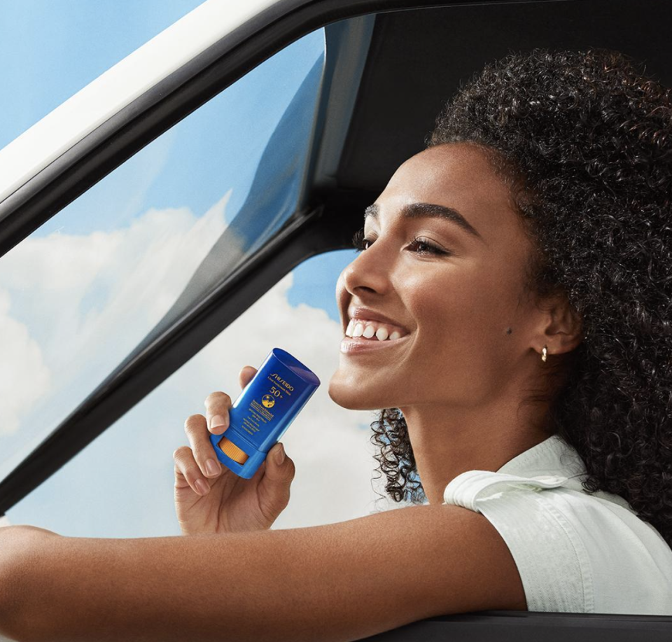 Woman in a car smiling at a blue card she's holding up to window, implying contactless payment