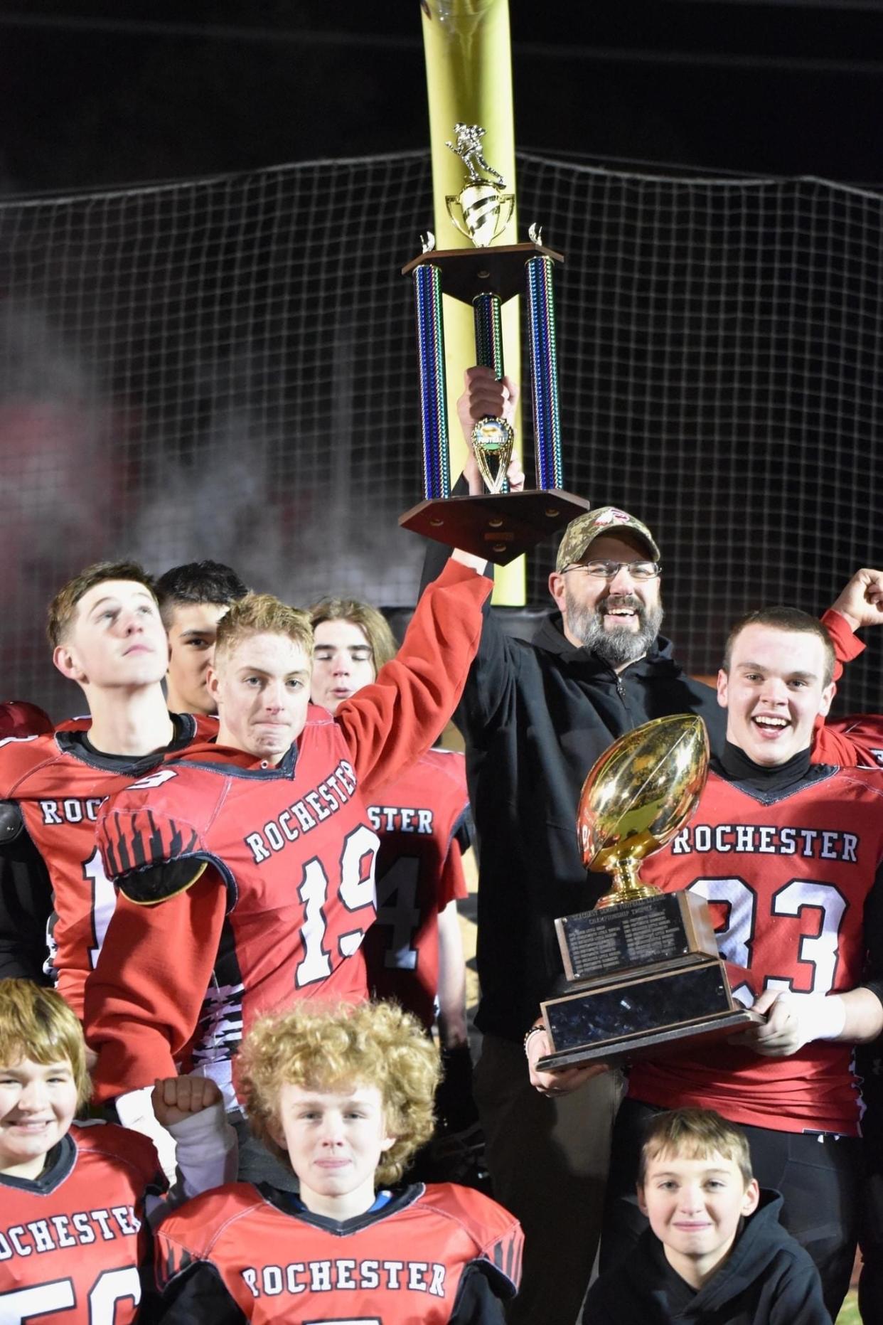 Rochester Red Raider Riley Rup (19) and his father and team head coach Tom Rup raise the championship trophy after beating Andover, Massachusetts, 24-21 on Saturday in the Northeast Junior High Football League championship at Souhegan High School.