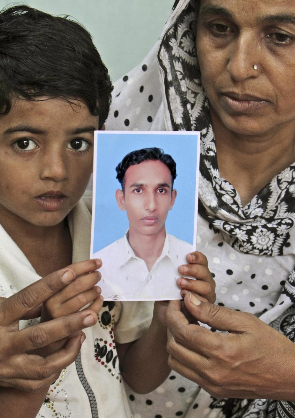 In this Friday, Oct. 19, 2012, photo, a portrait of Pakistani Muhammad Shehbaz, who was killed in a fire at a garment factory last September, is held by his mother and brother, at the family's house in Karachi, Pakistan. At the only morgue in Pakistan's largest city lie the blackened remains of 32 people killed in one of the worst industrial accidents in the country's history, wrapped in white plastic body bags waiting for DNA tests to determine who they are and where they belong. (AP Photo/Fareed Khan)