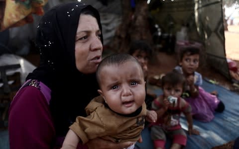 A Syrian woman with her baby is seen inside a makeshift tent among olive trees on their way from Syrias de-escalation zones in Idlib - Credit: Muhammed Said/Anadolu Agency via Getty Images