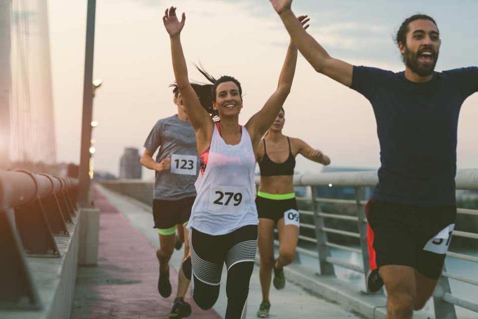 A group of runners smile with their arms raised as they cross a bridge