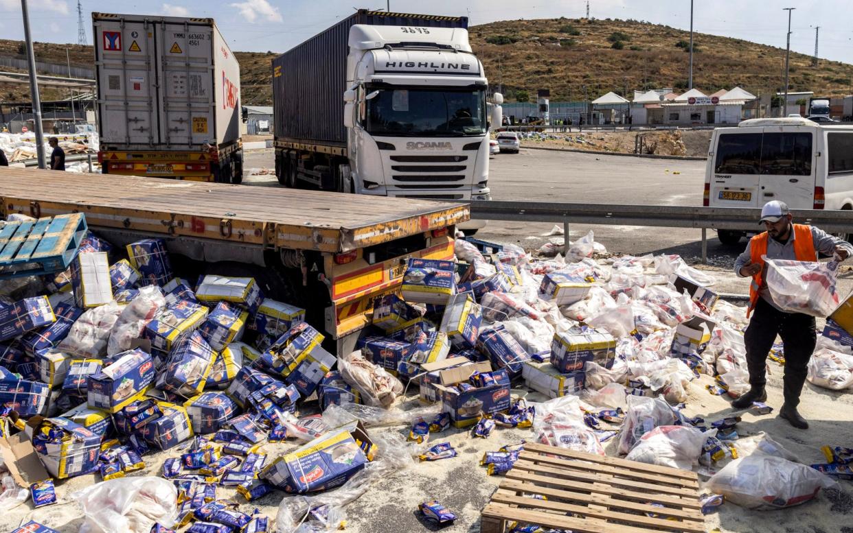 A worker clears spilled goods from damaged trailer trucks that were carrying humanitarian aid on the Israeli side of the Tarqumiyah crossing with the West Bank, on Monday