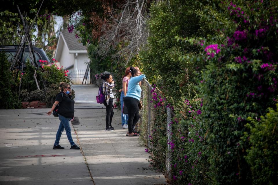 People lean on a fence, looking at a crash scene.