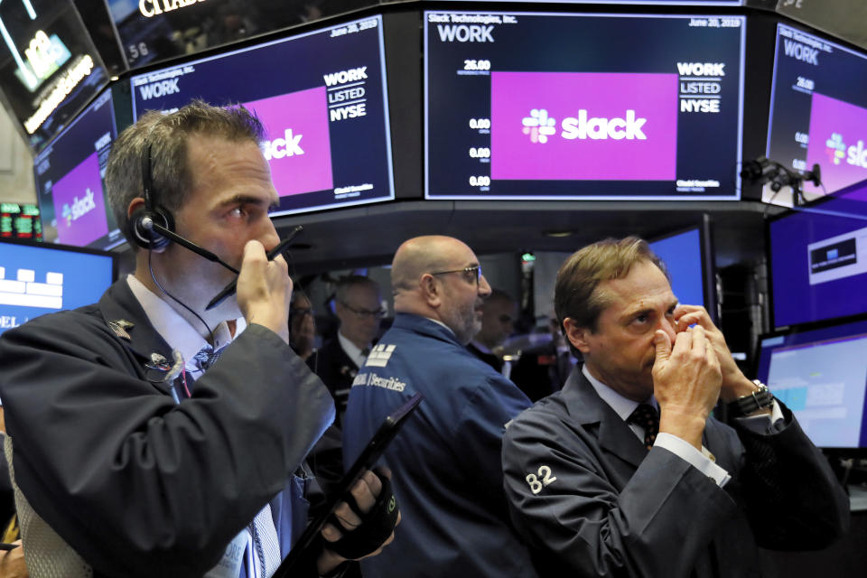 Traders Gregory Rowe, left, and Dudley Devine, right, talk into their mobile phones on the floor of the New York Stock Exchange as they wait for the Slack Technologies IPO to begin trading, Thursday, June 20, 2019. (AP Photo/Richard Drew)