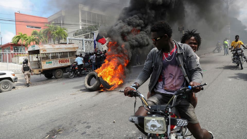 People drive past a burning blockade as demonstrators hold a protest calling for the resignation of Haitian Prime Minister Ariel Henry outside the Canadian Embassy, in Port-au-Prince, Haiti February 25 2024. - Ralph Tedy Erol/Reuters
