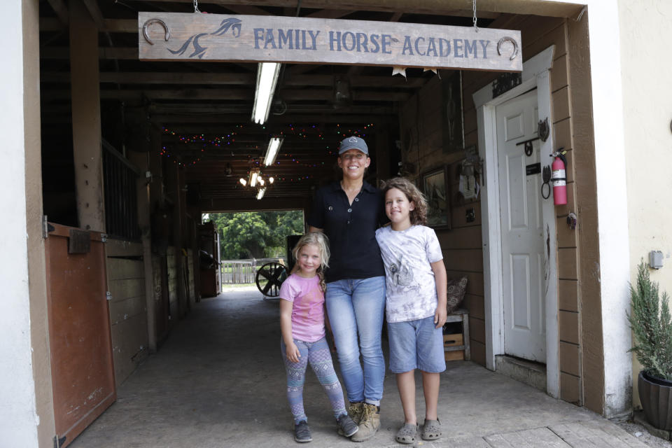 Timea Hunter poses for a photograph with her children Lena, left, and Liam, right, at the Family Horse Academy, where she is hoping to organize education for a group of children during the coronavirus pandemic, Friday, July 31, 2020, in Southwest Ranches, Fla. Confronting the likelihood of more distance learning, families across the country are turning to private tutors and "learning pods" to ensure their children receive some in-person instruction. The arrangements raise thorny questions about student safety, quality assurance, and inequality. (AP Photo/Lynne Sladky)