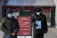 A man wearing a face mask to help protect from the coronavirus walks by a security guard holding a health code notice at an entrance gate to a park in Beijing, Tuesday, Jan. 25, 2022. Hong Kong has already suspended many overseas flights and requires arrivals be quarantined, similar to mainland China's "zero-tolerance" approach to the virus that has placed millions under lockdowns and mandates mask wearing, rigorous case tracing and mass testing. (AP Photo/Andy Wong)