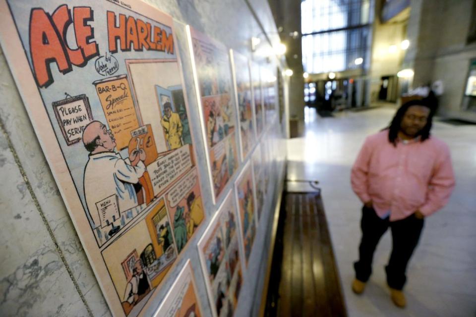 In this Wednesday, Feb. 5, 2014 photo, Chay Tyler stands near the pages from the single issue of “All-Negro Comics” that is part of an exhibit on display at the City/County building in downtown Pittsburgh. The exhibit chronicles some early African American artists and a publisher who started to break the comic color barrier in the 1930s and 1940s. Tyler is a program coordinator for the city Department of Parks and Recreation and helped curate the exhibit. (AP Photo/Keith Srakocic) (AP Photo/Keith Srakocic)