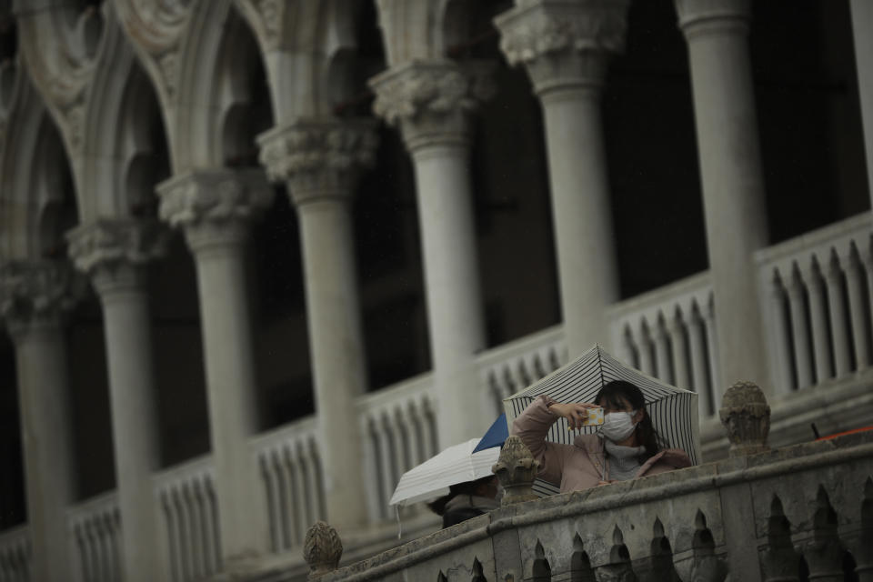 Tourists wearing protective masks take photographs in Venice, Sunday, March 1, 2020. Italian tourism officials are worrying a new virus could do more damage to their industry than the Sept. 11 terror attacks as the country's confirmed cases surpassed 1,000. (AP Photo/Francisco Seco)