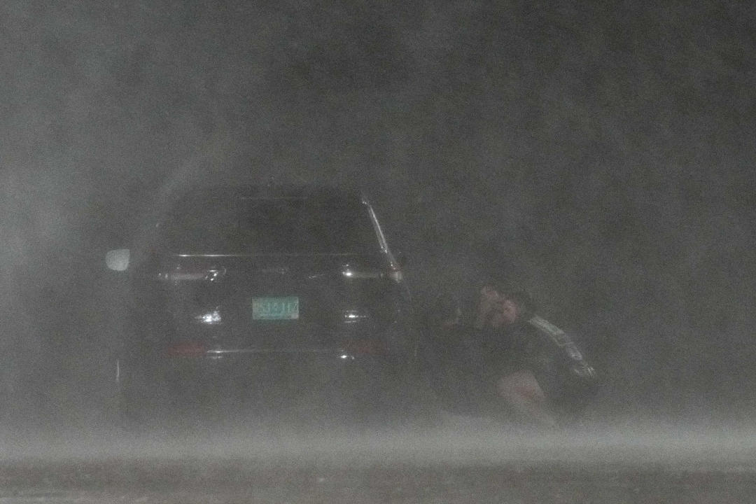 A group of people crouched down hiding behind a car to shield themselves from wind and rain from Hurricane Beryl.