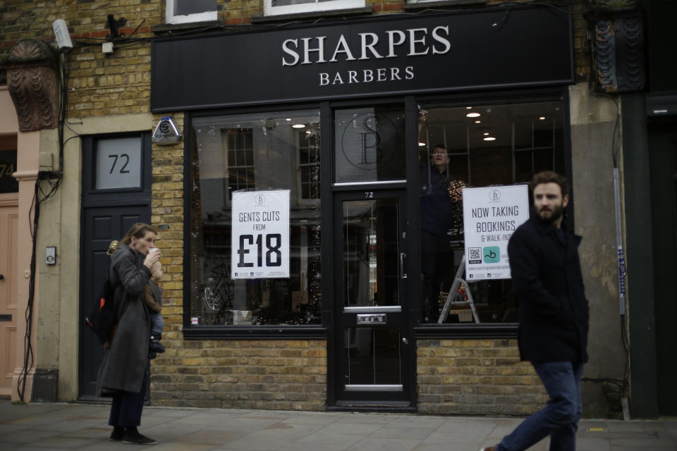 Barber Matthew Jones puts up Christmas lights in the front windows of his 'Sharpes Barbers' in readiness for when England's second coronavirus lockdown is due to end on December 2, and he will be allowed to reopen for business, on Broadway Market in Hackney, east London, Tuesday, Nov. 17, 2020. The London barber shop was busy cutting hair, laughing with colleagues and customers, when the news that the business would have to close because of the coronavirus for the second time landed. (AP Photo/Matt Dunham)