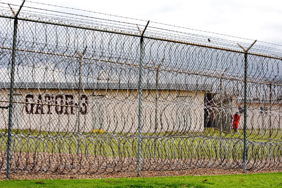 FILE - A prisoner, far right, is seen behind layers of wire razor fencing at the Louisiana State Penitentiary, the Angola Prison, in Angola, La., April 22, 2009. A controversial transfer of juvenile prisoners to a temporary facility at Louisiana’s sprawling high security prison farm for adult convicts involves a shuffle of youths to and from four different lockups around the state, officials said Thursday, Oct. 20, 2022. (AP Photo/Judi Bottoni, File)