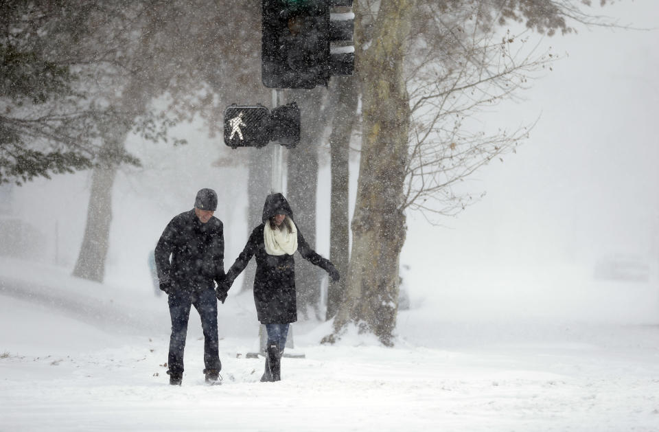 Andrew Loza, left, walks down a snow-covered sidewalk with Emily Olfson Sunday, Jan. 5, 2014, in St. Louis. Heavy snow continues to fall Sunday with forecasters calling for up to a foot (30 centimeters) in eastern Missouri and parts of central Illinois followed by bitter cold. (AP Photo/Jeff Roberson)