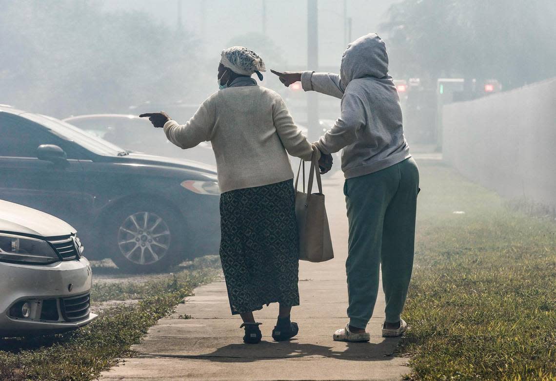 Francilia Jean, left, is assisted as she points toward a fire that engulfs her two-story apartment building at 395 NW 177th St. on Saturday morning, Jan. 28, 2023.