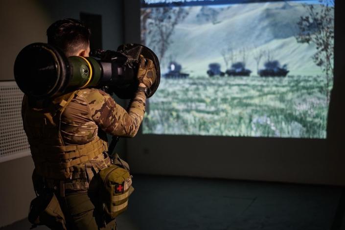 In a training center, a soldier aims an antitank weapon at a computer-projected image of a Russian tank.