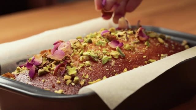 Sprinkling chopped pistachios and dried rose petals over cake