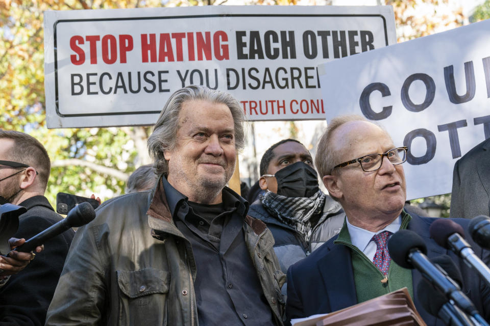 Former White House strategist Steve Bannon, smiling, and his attorney David Schoen speak to reporters in front of a sign reading 