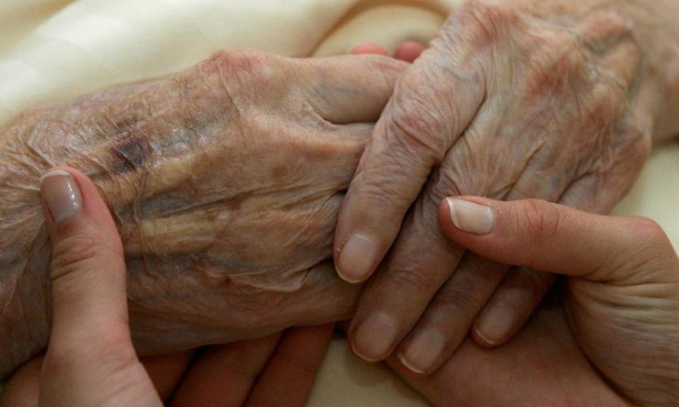 A young carer holds the hands of an elderly woman