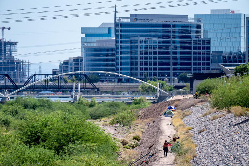 People walk near a homeless encampment along the Rio Salado riverbed in Tempe on Aug. 31, 2022. Tempe gave notice for people living in the river bottom to vacate by Aug. 31.