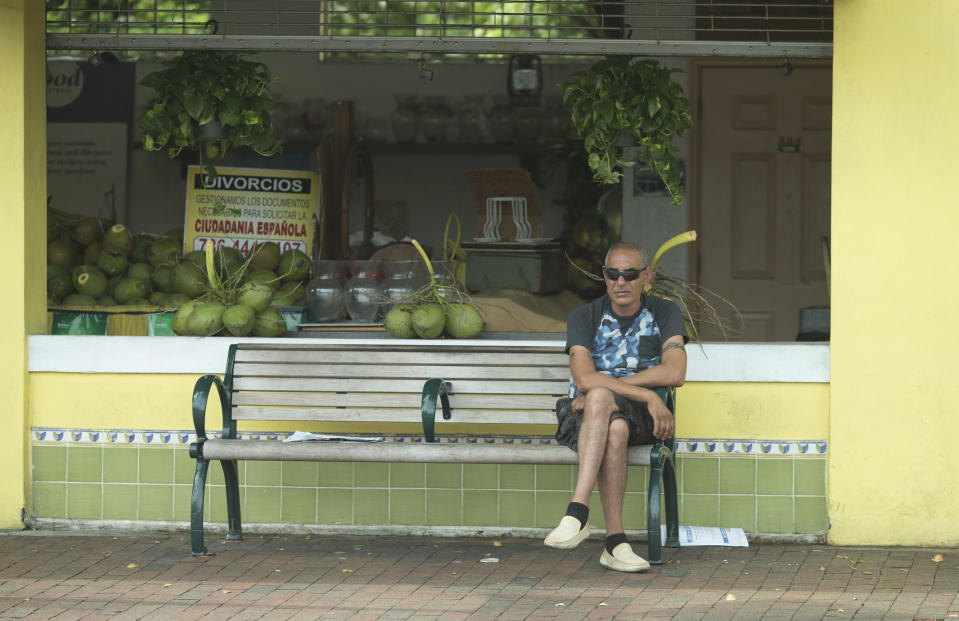 This May 2, 2014 photo shows a man sitting on a bench on Calle Ocho (Eighth Street) bench in front of the Los Pinarenos Fruteria in Miami's Little Havana. Once a refuge for Cuban exiles rekindling the tastes and sounds a lost home, today Miami’s Little Havana is a mosaic of cultures and a popular tourist destination. (AP Photo/J Pat Carter)