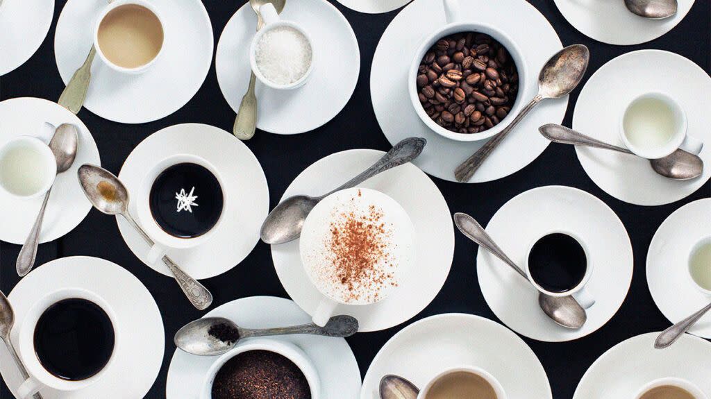 A flat lay of ceramic cups containing ingredients to coffee and different types and flavors of coffee drinks