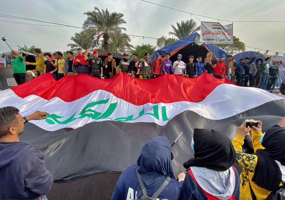 CORRECTS TO REMOVE REFERENCE TO INCIDENT INVOLVING GUNMAN - Anti-government protesters hold a huge Iraqi flag as they gather in Tahrir Square during ongoing protests in Baghdad, Iraq, Thursday, Dec. 12, 2019. (AP Photo/Khalid Mohammed)