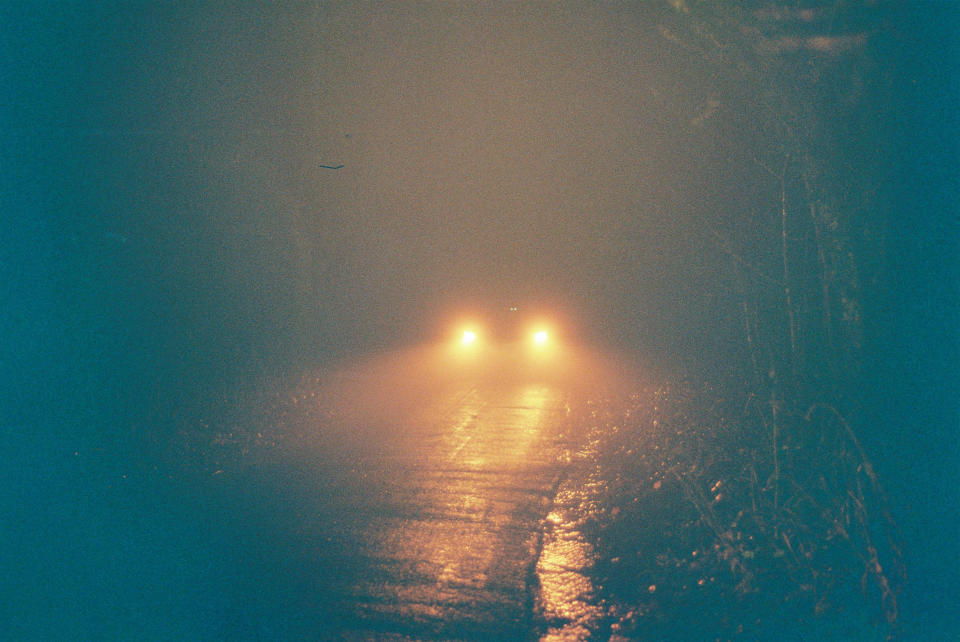 A car is driving through a foggy, deserted road