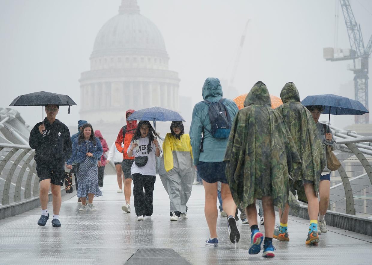 People walking along the Millennium Bridge in London during a rain shower, Wednesday 2 August (PA)