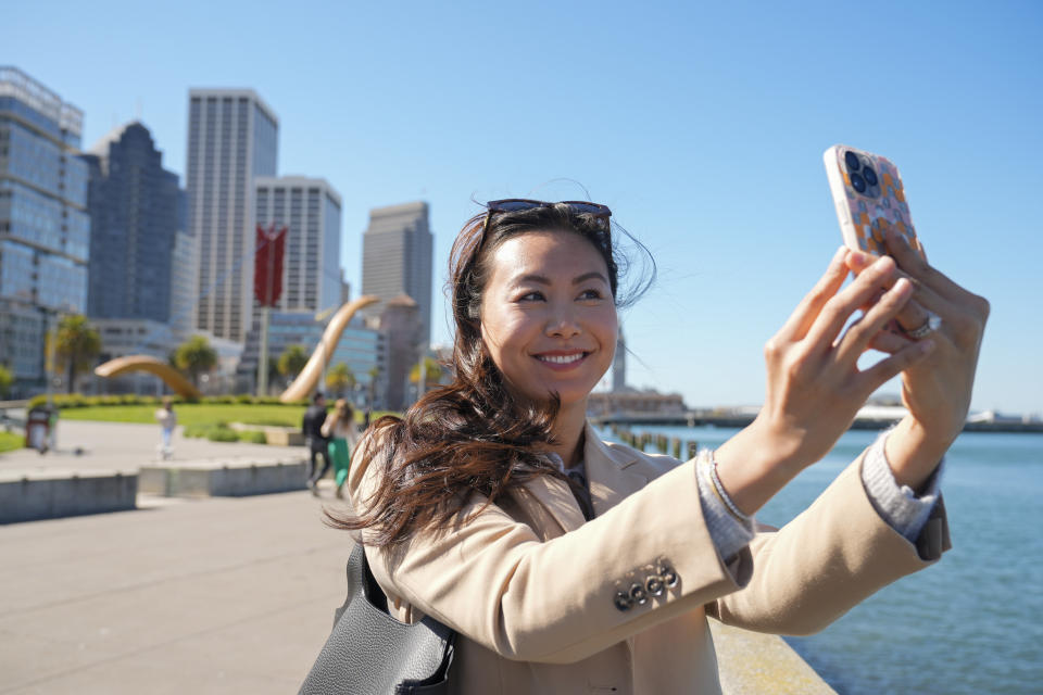 Content creator Cynthia Huang Wang works along the Embarcadero in San Francisco, Monday, April 8, 2024. Despite a strong job market, there are still thousands of people who have found themselves out of work across industries stretching from tech to retail to media. But rather than trying to find another job in their old role, some workers are turning to online content creation. (AP Photo/Eric Risberg)