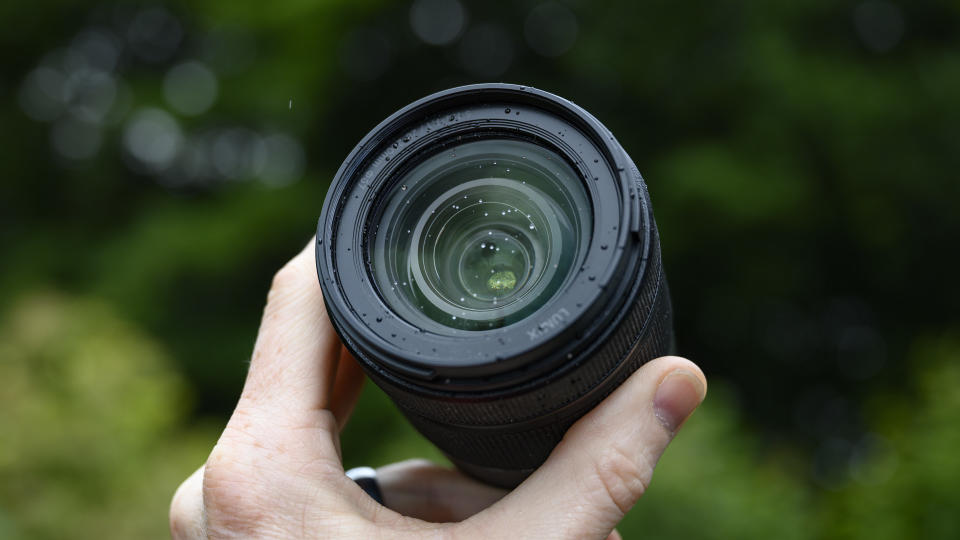 Panasonic Lumix S 28-200mm travel lens in the hand with leafy background and light rain