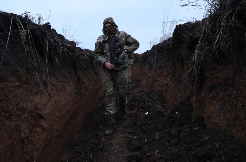 A Ukrainian soldier walks through trenches near Bakhmut, Ukraine, with a grey sky above him