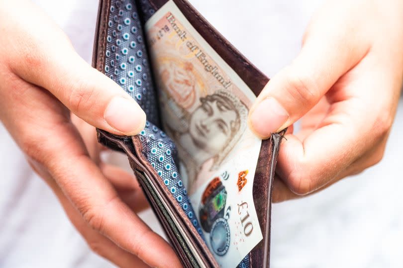 Two hands opening a wallet with a £10 note inside