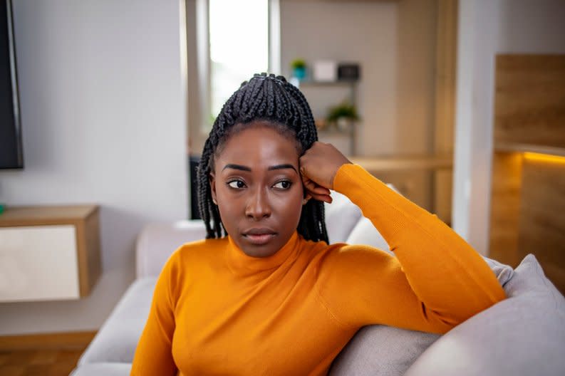 A person who looks stressed and deep in thought while sitting on the couch.