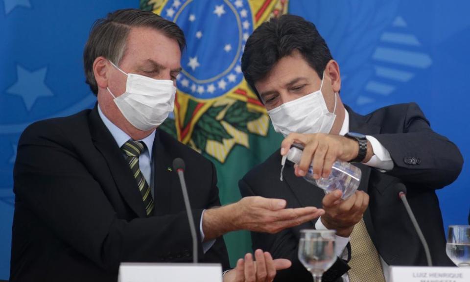 Luiz Henrique Mandetta gives hand sanitiser to Jair Bolsonaro during a press conference in Brasília on 18 March.