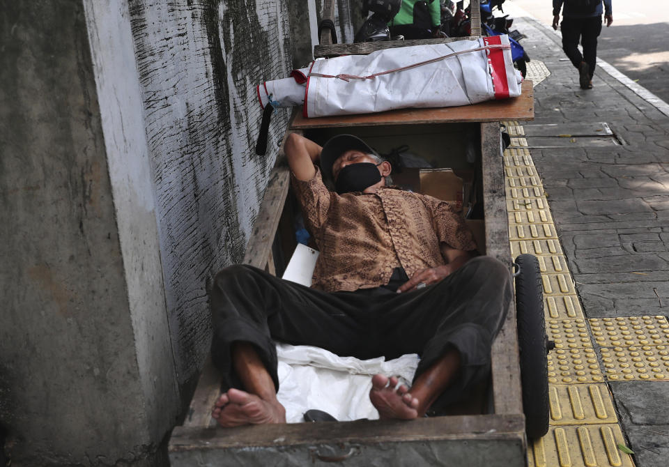 A man wearing a face mask takes a nap on his cart in Jakarta, Indonesia, Tuesday, June 22, 2021. Indonesia, the world's fourth most populous country, has seen COVID-19 infections surge in recent weeks, a climb that has been blamed on travel during last month's Eid al-Fitr holiday as well as the arrival of new virus variants, such as the the Delta version first found in India. (AP Photo/Tatan Syuflana)
