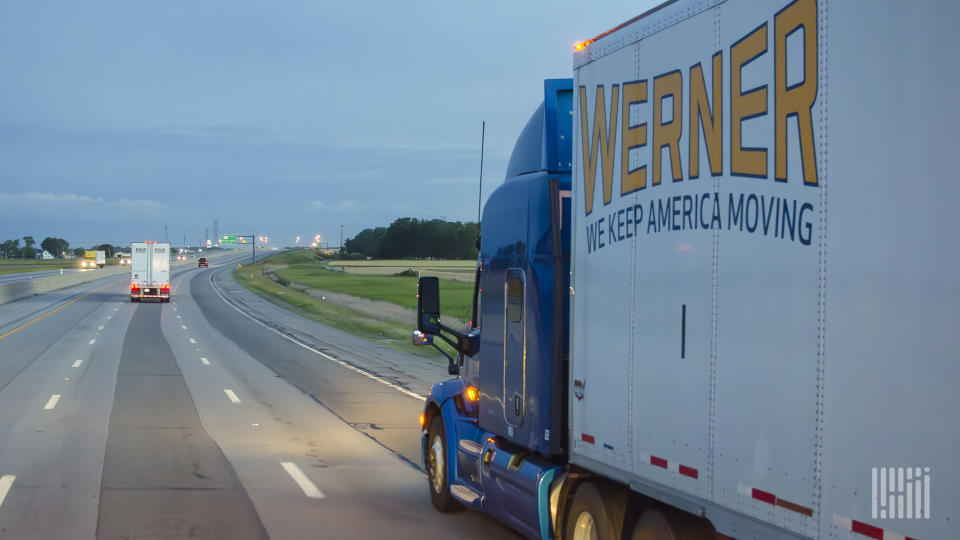 A blue Werner tractor pulling a white Werner trailer at night on a highway