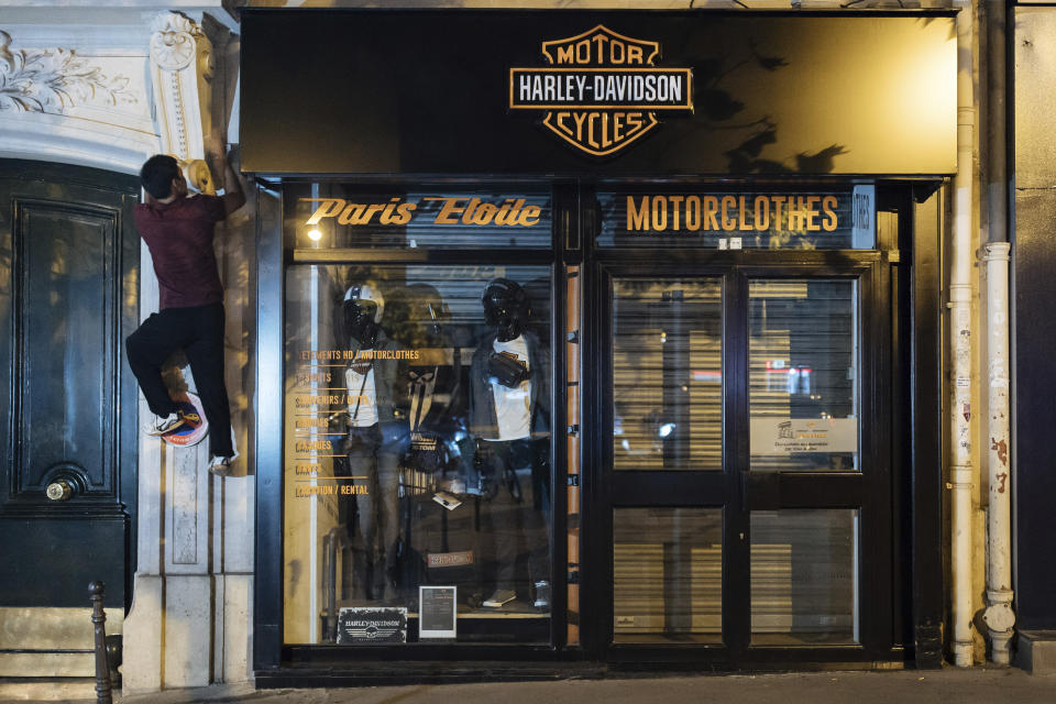 Kevin Ha from the collective "On the Spot" climbs to turn off the lights of a store in Paris, Friday, July 29, 2022. Engineer Kevin Ha and his equally nimble friends had been acting against wasteful businesses in Paris long before Russia started cutting energy supplies to Europe in a battle of wills over Moscow's invasion of Ukraine. As such, the campaigners were precursors of the energy economy drive becoming all the rage in France, Germany and elsewhere. (AP Photo/Lewis Joly)