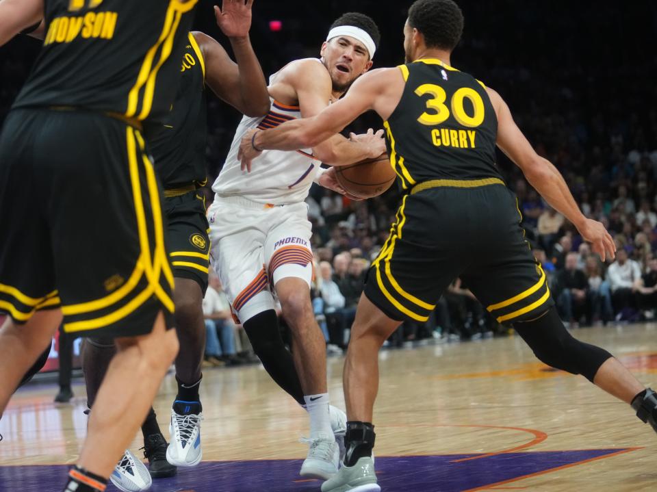 Nov 22, 2023; Phoenix, AZ, USA; Phoenix Suns guard Devin Booker (1) drives in to the lane as Golden State Warriors guard Stephen Curry (30) defends at Footprint Center.