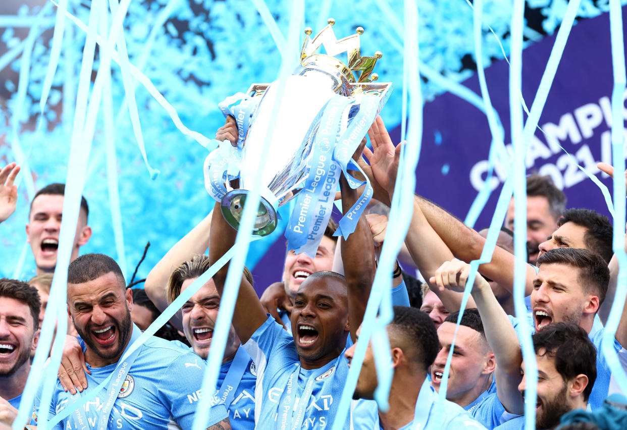 Manchester City's Fernandinho lifts the Premier League trophy as he celebrates with teammates.